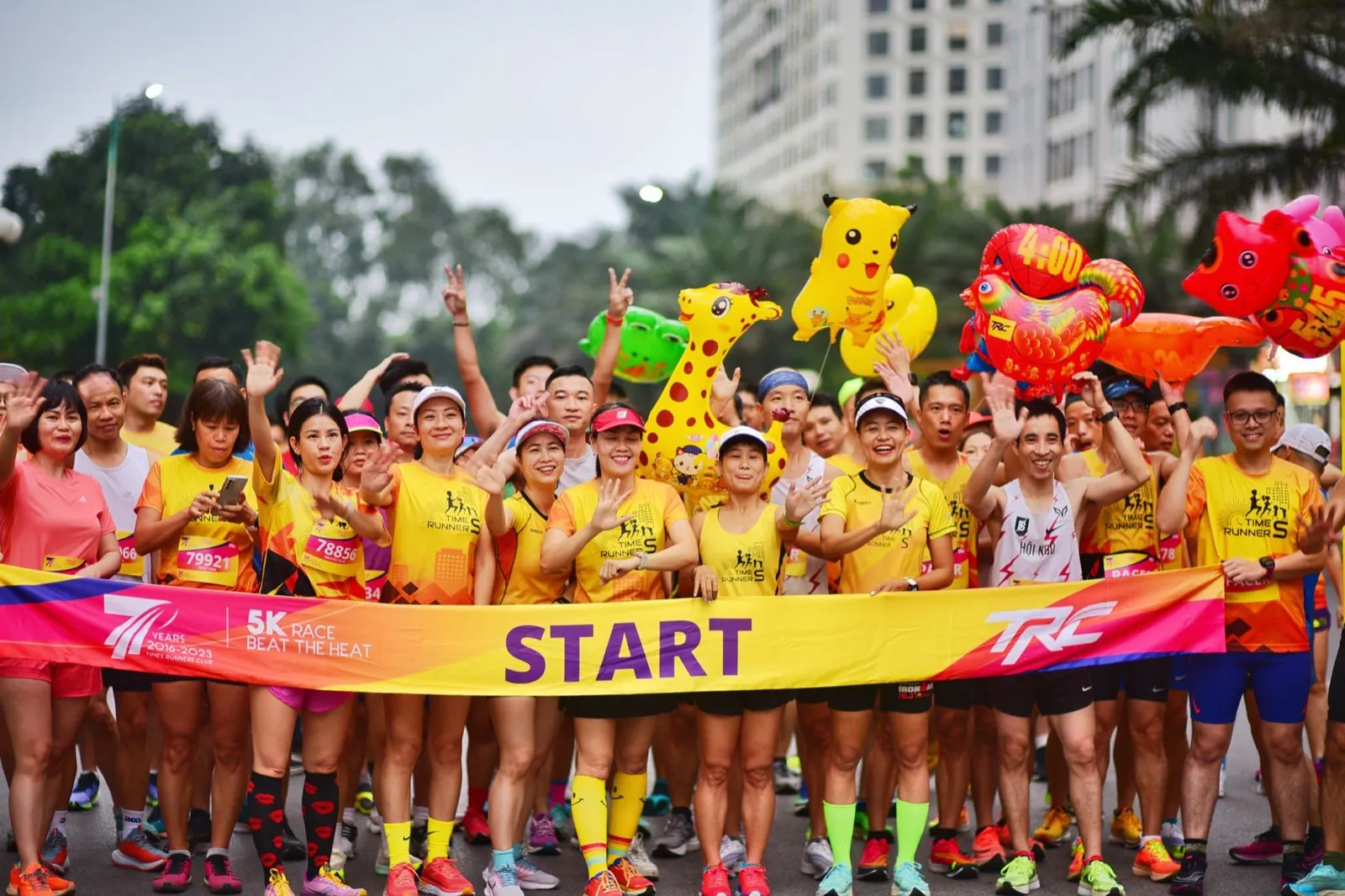 一群穿黃橘色跑衣的跑者在 5K 起跑線前揮手,手上拿著卡通造型氣球,舒跑杯 5K 挑戰組